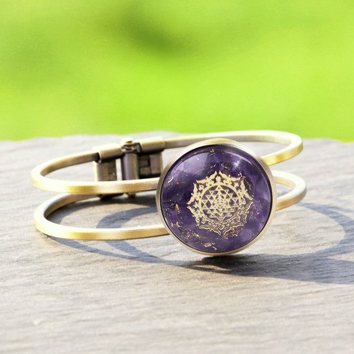An orgonite bracelet with a brushed copper bangle. Amethyst stones and gold foil shavings surround a sacred Sri Yantra energy patch.