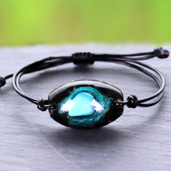 An orgonite bracelet that resembles a galaxy, with Obsidian surrounding a single Turquoise stone.