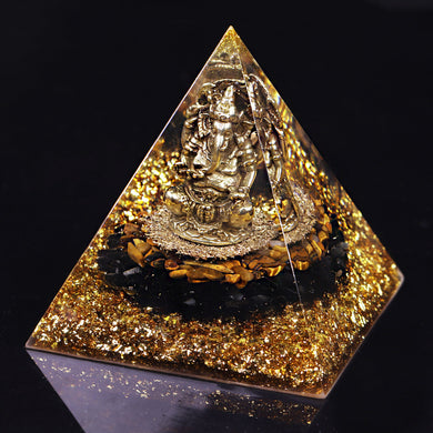 An orgonite pyramid with Tiger's Eye and Obsidian stones. Features a central metal statue of Ganesh and gold foil shavings.