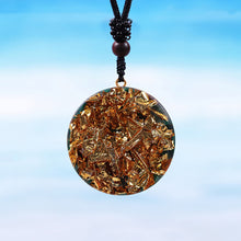 Load image into Gallery viewer, The back of an orgonite necklace featuring golden copper shavings embedded in a smooth, polished resin surface, hanging against a gradient blue sky background.