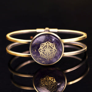 An orgonite bracelet with a brushed copper bangle. Amethyst stones and gold foil shavings surround a sacred Sri Yantra energy patch.