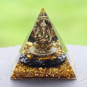 An orgonite pyramid with Tiger's Eye and Obsidian stones. Features a central metal statue of Ganesh and gold foil shavings.