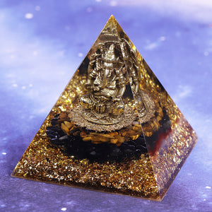 An orgonite pyramid with Tiger's Eye and Obsidian stones. Features a central metal statue of Ganesh and gold foil shavings.