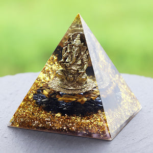 An orgonite pyramid with Tiger's Eye and Obsidian stones. Features a central metal statue of Ganesh and gold foil shavings.