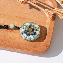 Load image into Gallery viewer, Top-down view of an orgonite pendant necklace with Amazonite and Lapis Lazuli stones and a Triskelion energy patch.